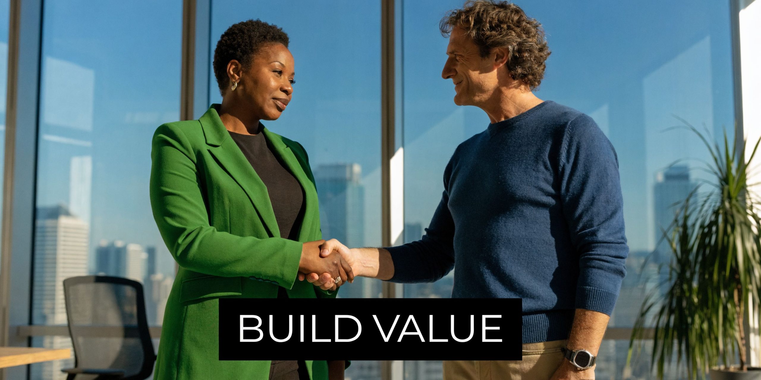 A professional woman in a green blazer and a man shaking hands in a bright, modern office.